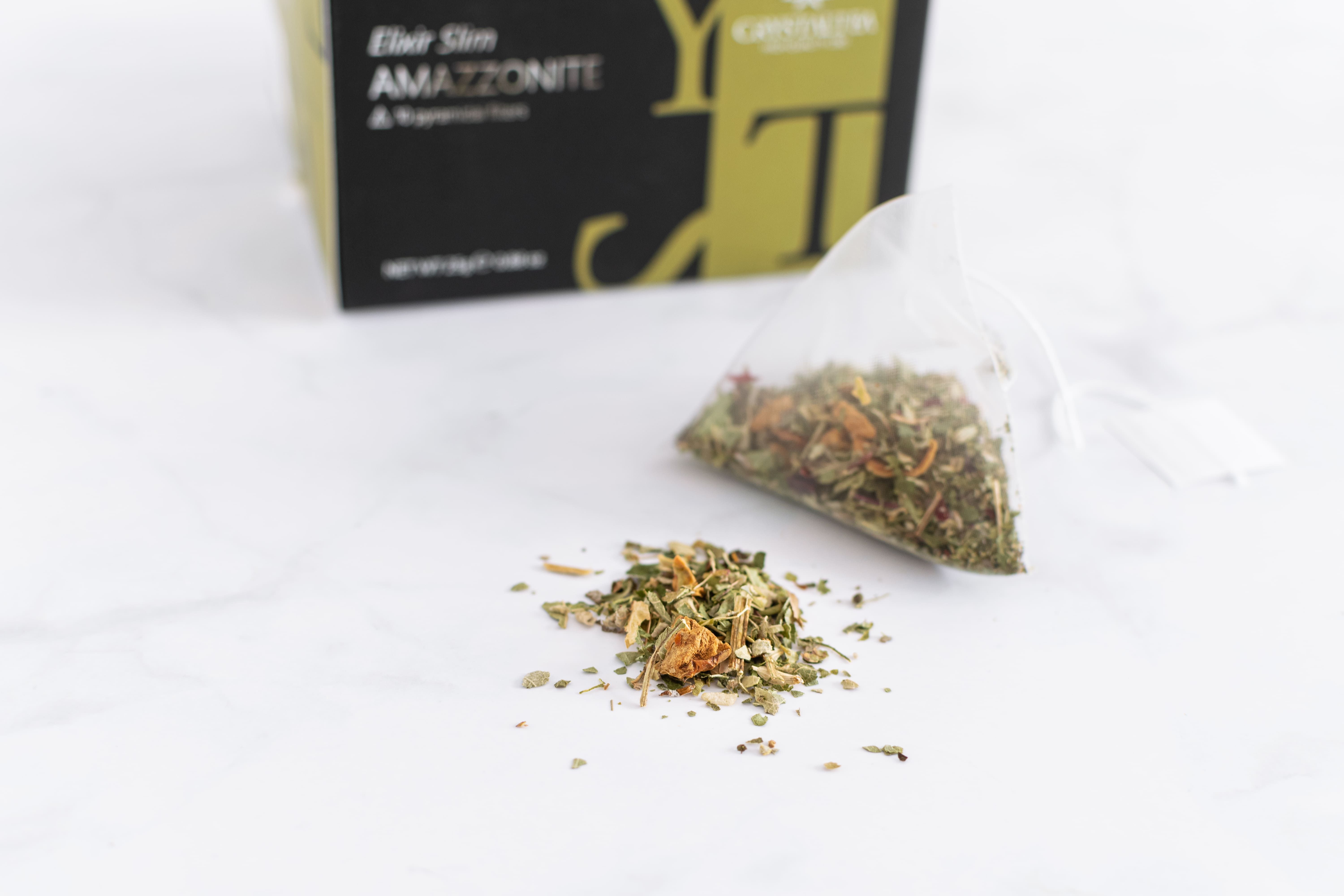 Bustina di tè con erbe e erbe sfuse accanto. Scatola con nome del prodotto e logo sullo sfondo.