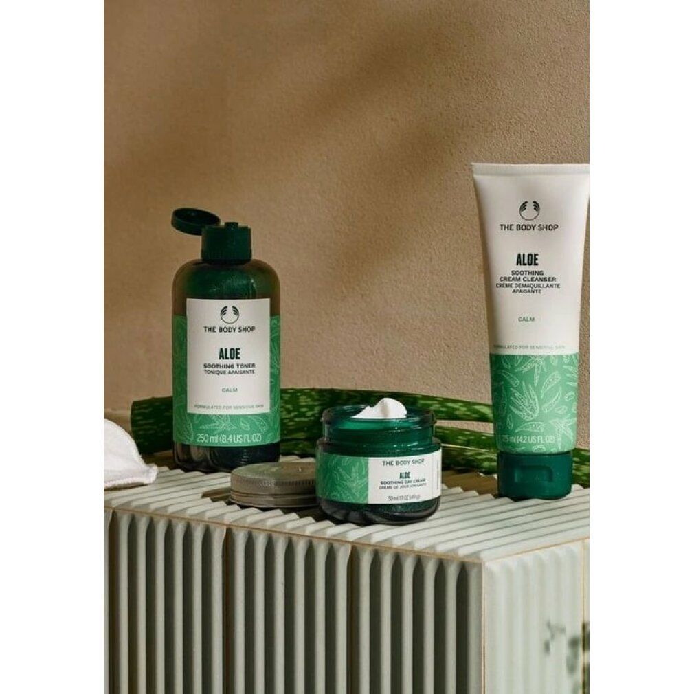 Tre prodotti: flacone, vasetto, tubo. Tutti verdi con etichetta bianca. Marchio: The Body Shop. Testo: Aloe. Su piedistallo bianco.