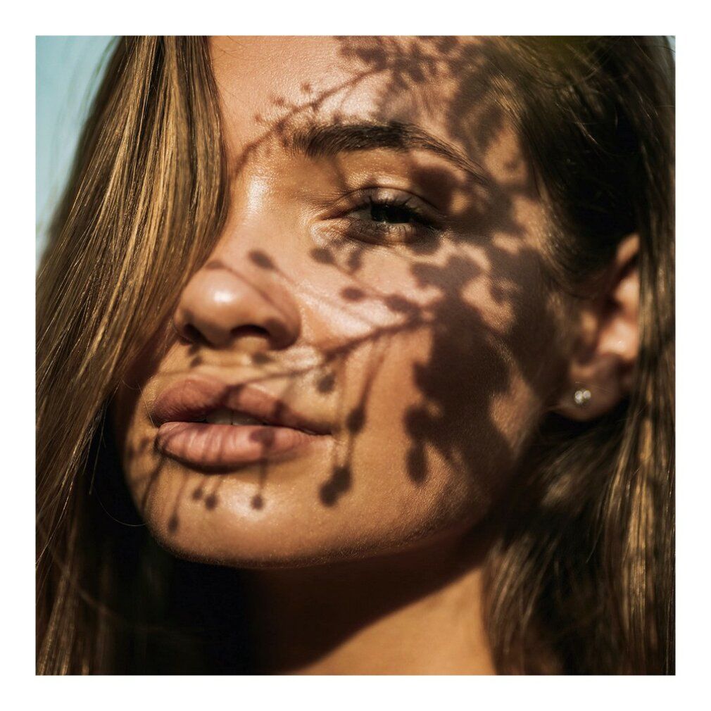 Ritratto di donna con ombre di foglie sul viso. Capelli chiari.