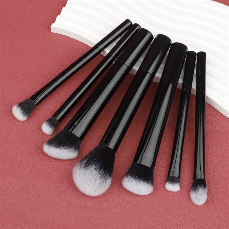 Sette pennelli per trucco neri con setole bianche, su sfondo bianco. Diverse forme.