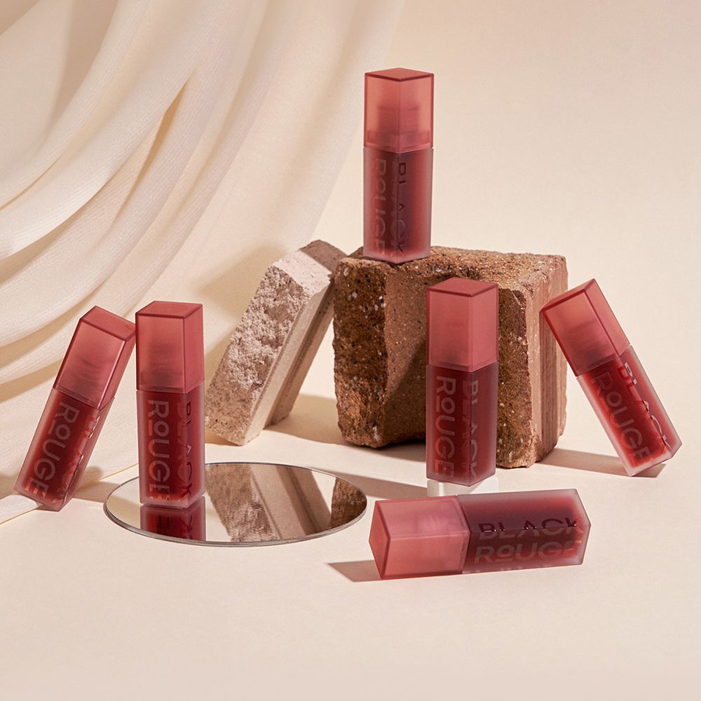 Diversi flaconi di lucidalabbra su una superficie. Tappi rosa, flaconi trasparenti. Scritta nera: BLACK ROUGE.
