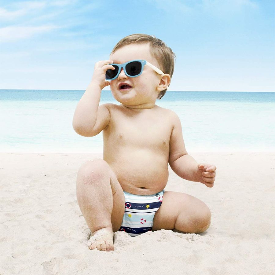 Bambino sulla spiaggia con occhiali da sole e costumino con salvagenti. Mare e cielo sullo sfondo.