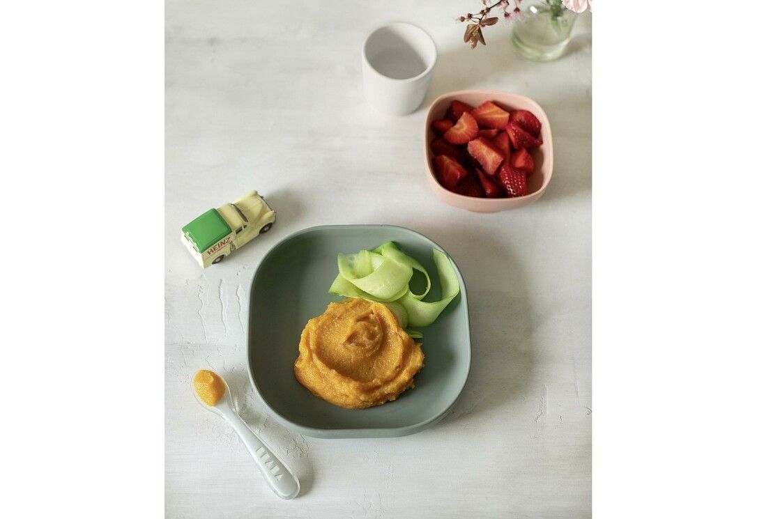 Piatto verde con verdure e purea. Ciotola rosa con fragole. Tazza bianca. Macchinina giocattolo.