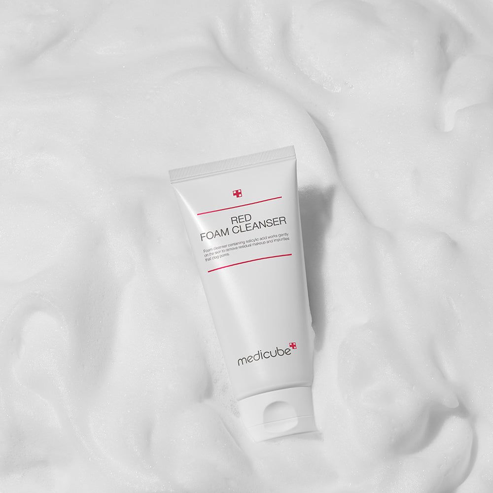 Tubo bianco con testo rosso: RED FOAM CLEANSER. Marchio: medicube. Immerso nella schiuma.