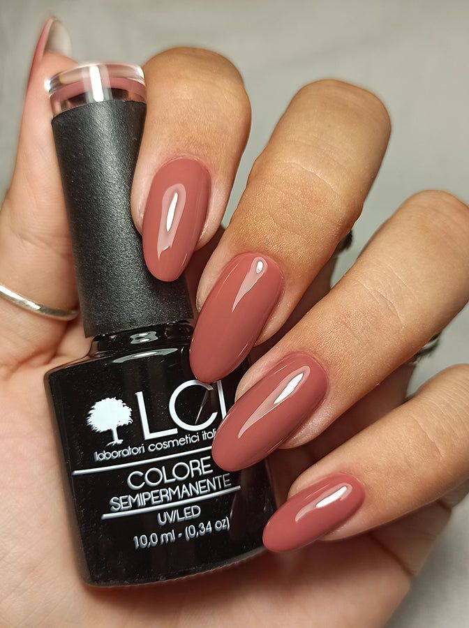 Mano con unghie smaltate e flacone di smalto. Unghie rosa-marrone. Flacone con tappo nero.