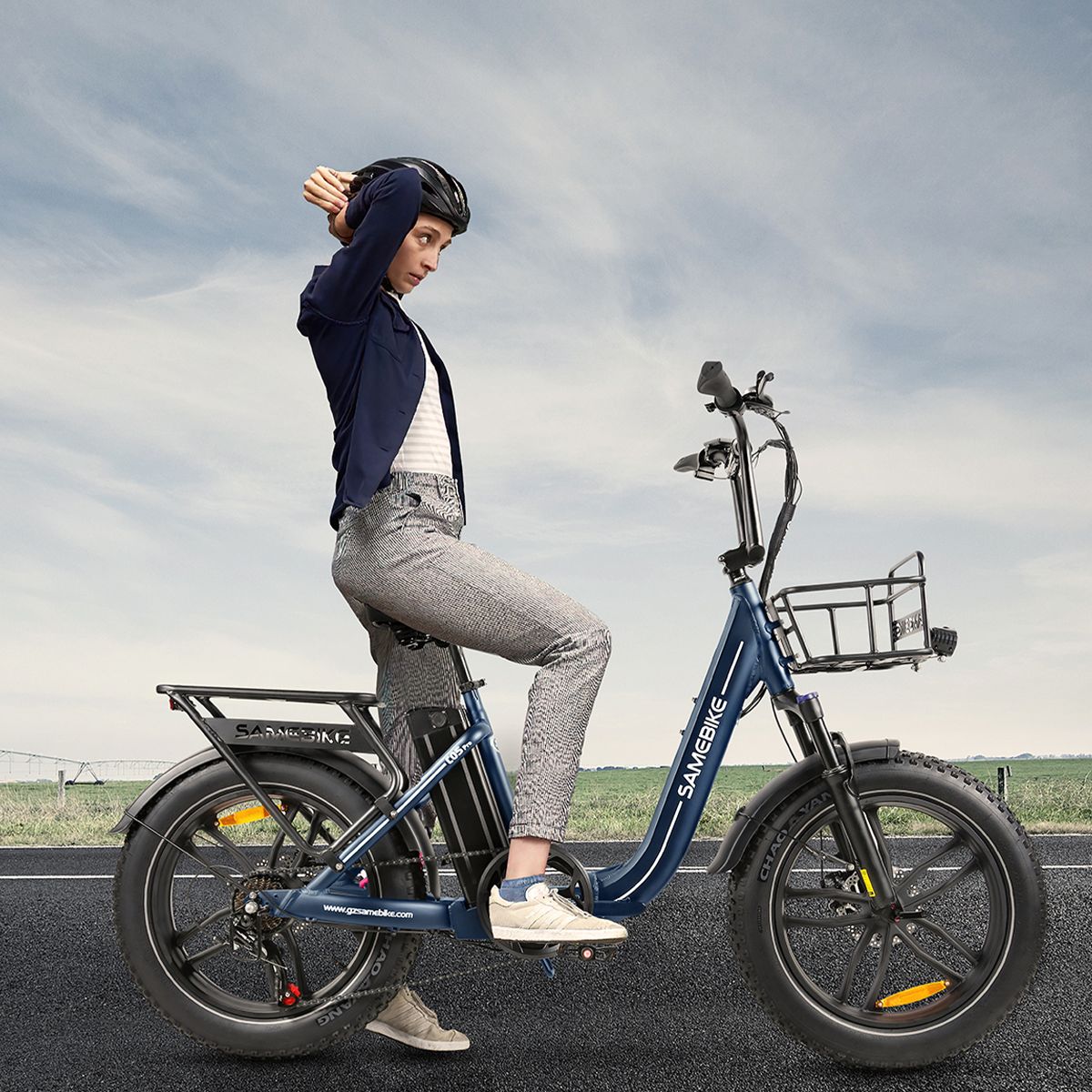 Persona seduta su e-bike SAMEBIKE C05 Pro blu. Casco, strada sullo sfondo. Marchio SAMEBIKE visibile.