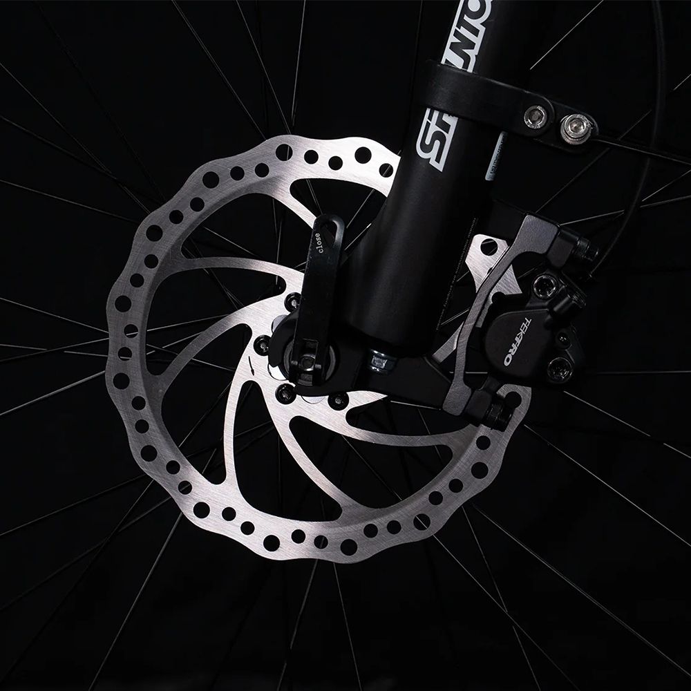 Primo piano del freno a disco di una bici. Disco freno argentato con pinza nera.