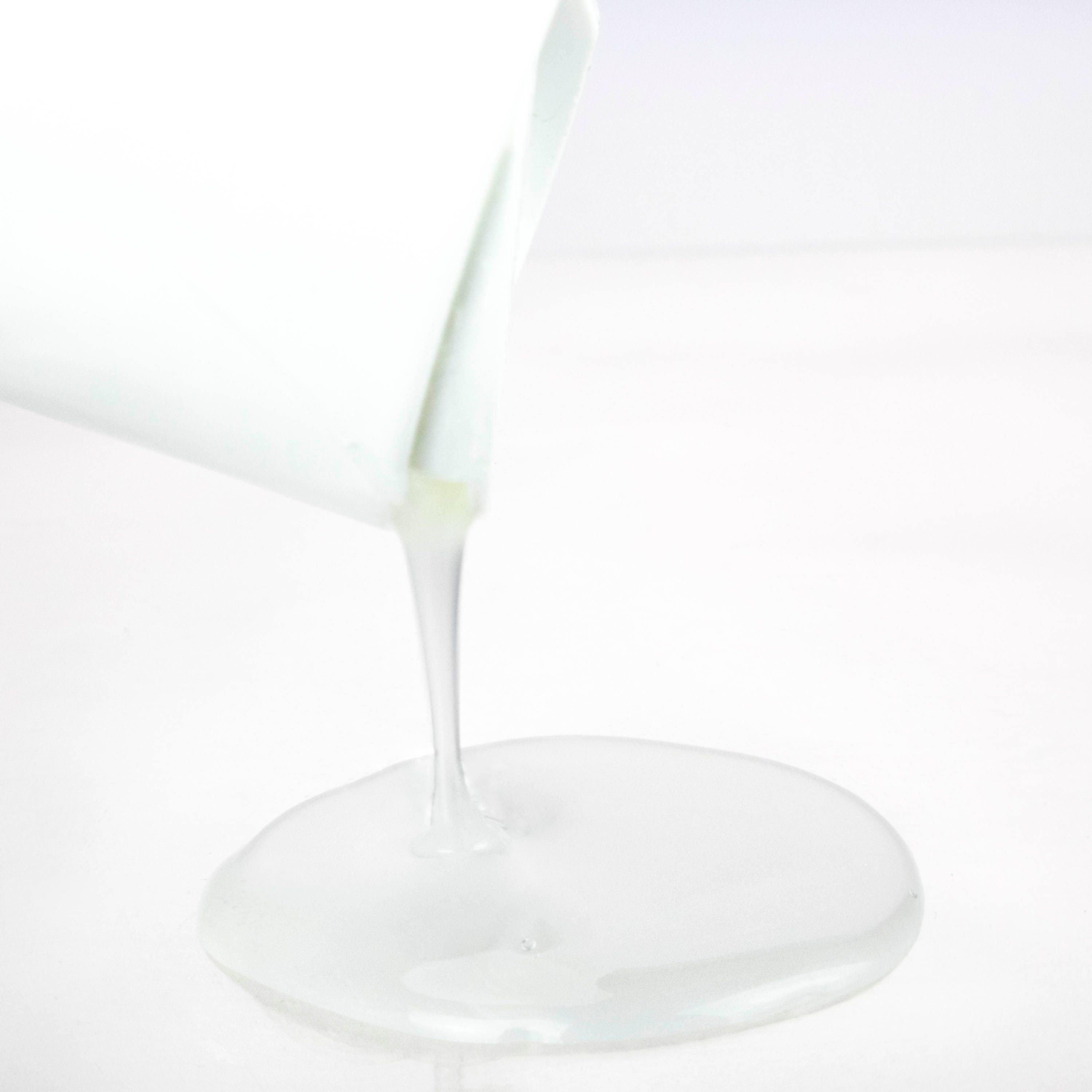 Liquido che fuoriesce da un flacone bianco. Il liquido è bianco e forma una pozza piatta su una superficie bianca.