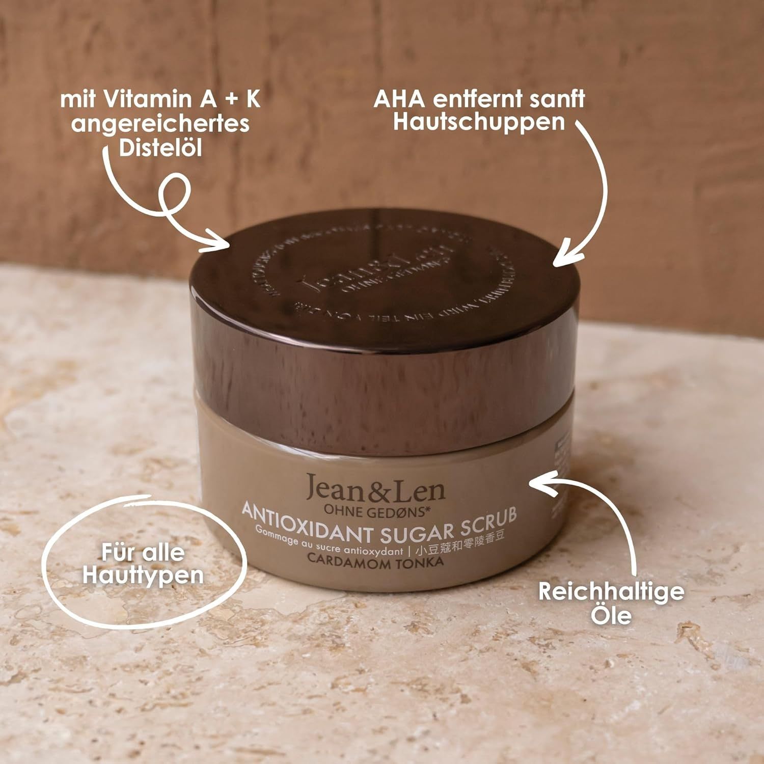 Vasetto con coperchio. Scritta: Jean & Len, Antioxidant Sugar Scrub, Cardamom Tonka. Frecce indicano ingredienti e proprietà.