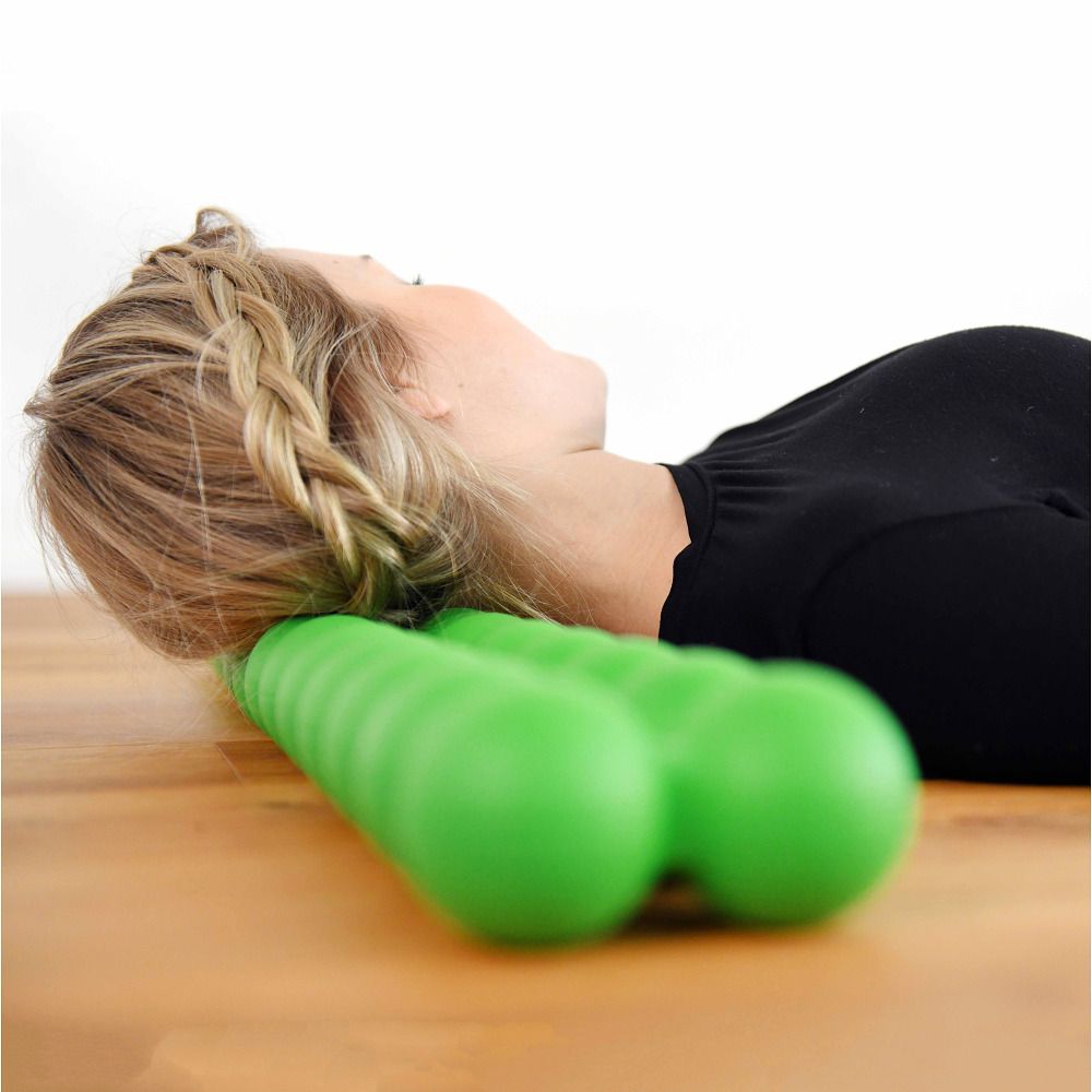Una donna è sdraiata con la testa su uno Spinefitter verde. Lo sfondo è chiaro e in legno.
