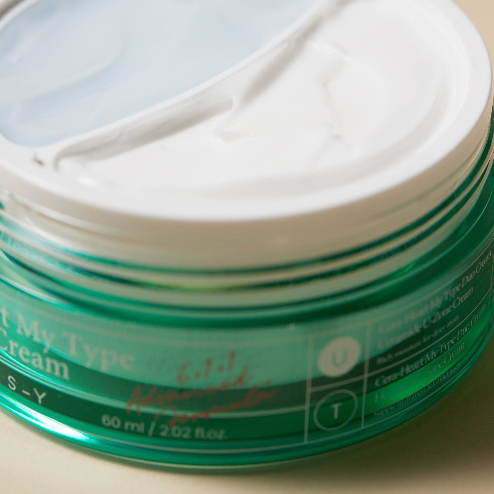 Primo piano di un vaso di crema verde con coperchio bianco. Scritta: Cera-Heart My Type Duo Cream. 60 ml.