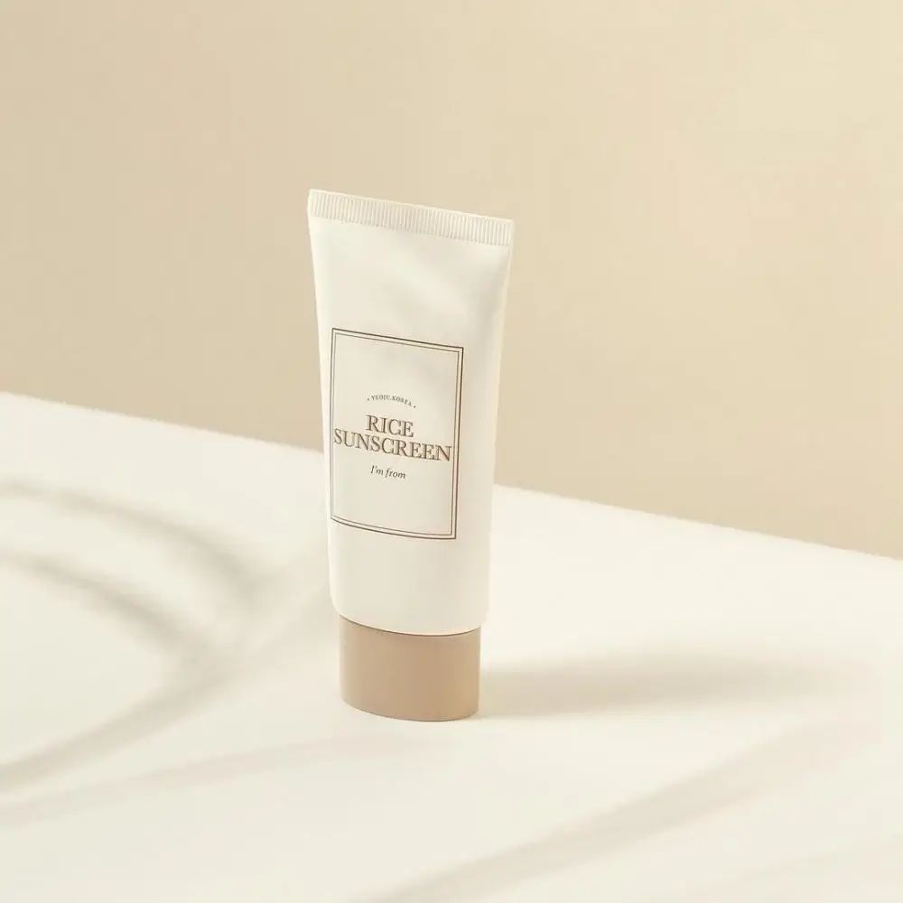 Tubo crema con scritta « Rice Sunscreen » e « I'm from ». Tappo beige su sfondo bianco.