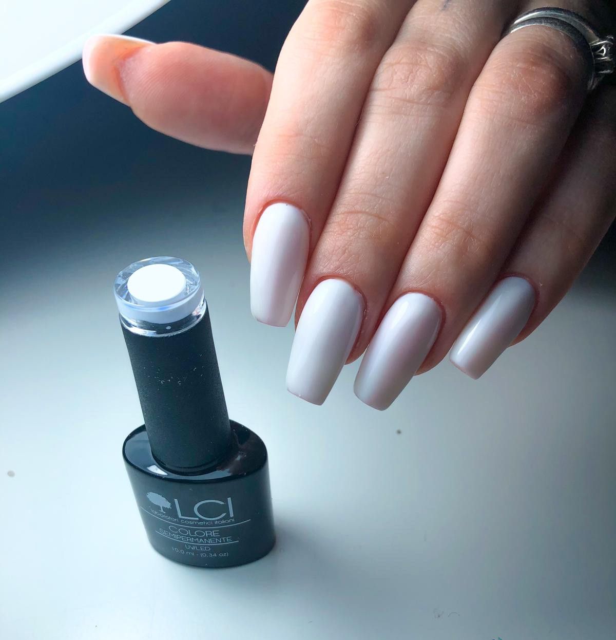 Mano con unghie bianche smaltate e flacone di smalto. Scritta: LCI, COLORE SEMIPERMANENTE.