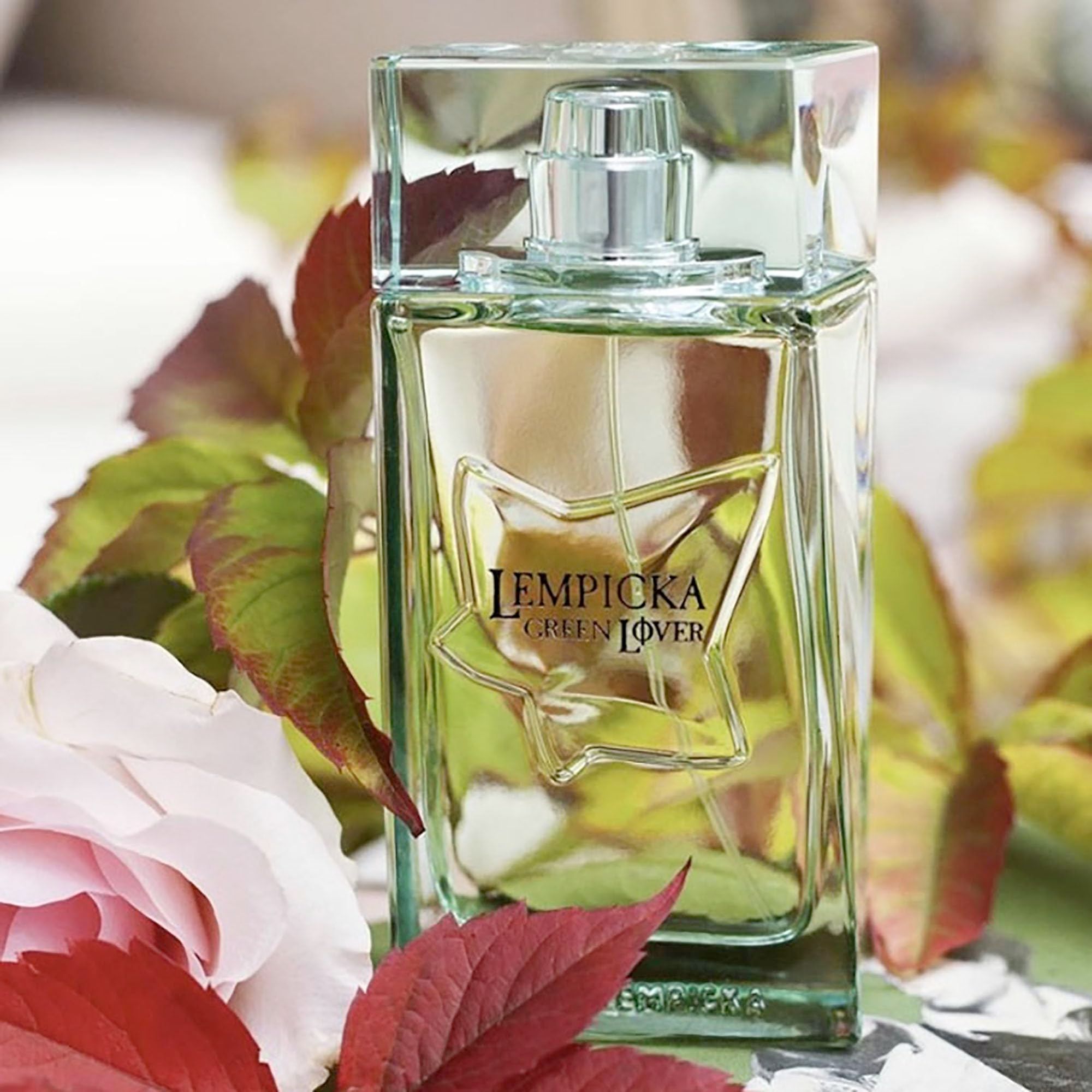 Flacone rettangolare con tappo verde. Scritta: LEMPICKA GREEN LOVER. Design a forma di stella. Circondato da foglie e fiori.