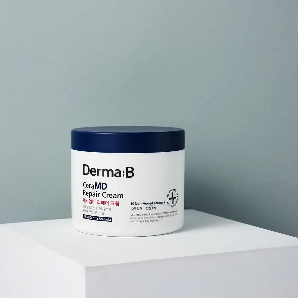 Vaso bianco con coperchio blu. Scritta: Derma:B CeraMD Repair Cream. Su superficie bianca, sfondo grigio.