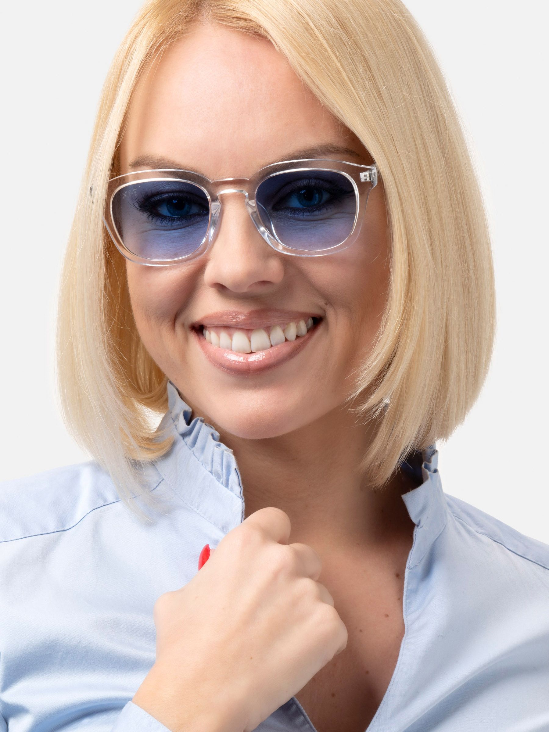 Donna bionda con occhiali da sole trasparenti e lenti blu. Sorride. Camicetta chiara.