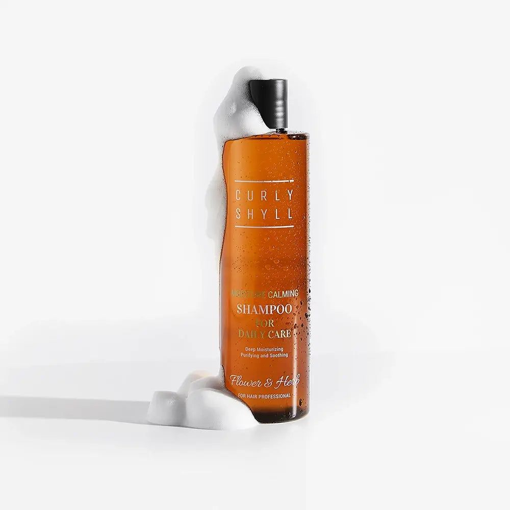 Bottiglia marrone con schiuma. Scritta: Curly Shyll, Moisture Calming Shampoo. Marchio: Flower & Herb.