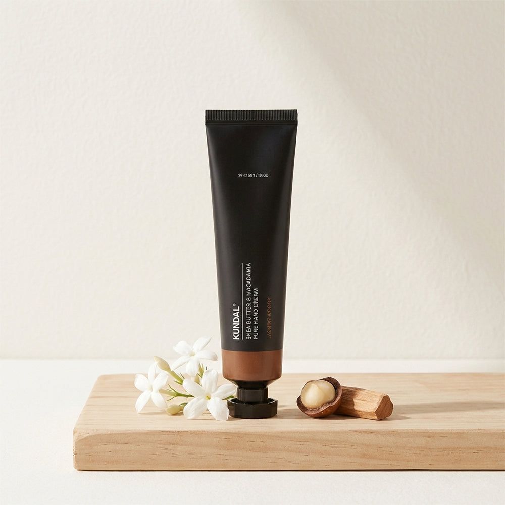 Tubo di crema mani KUNDAL con noci di macadamia e fiori su tagliere.