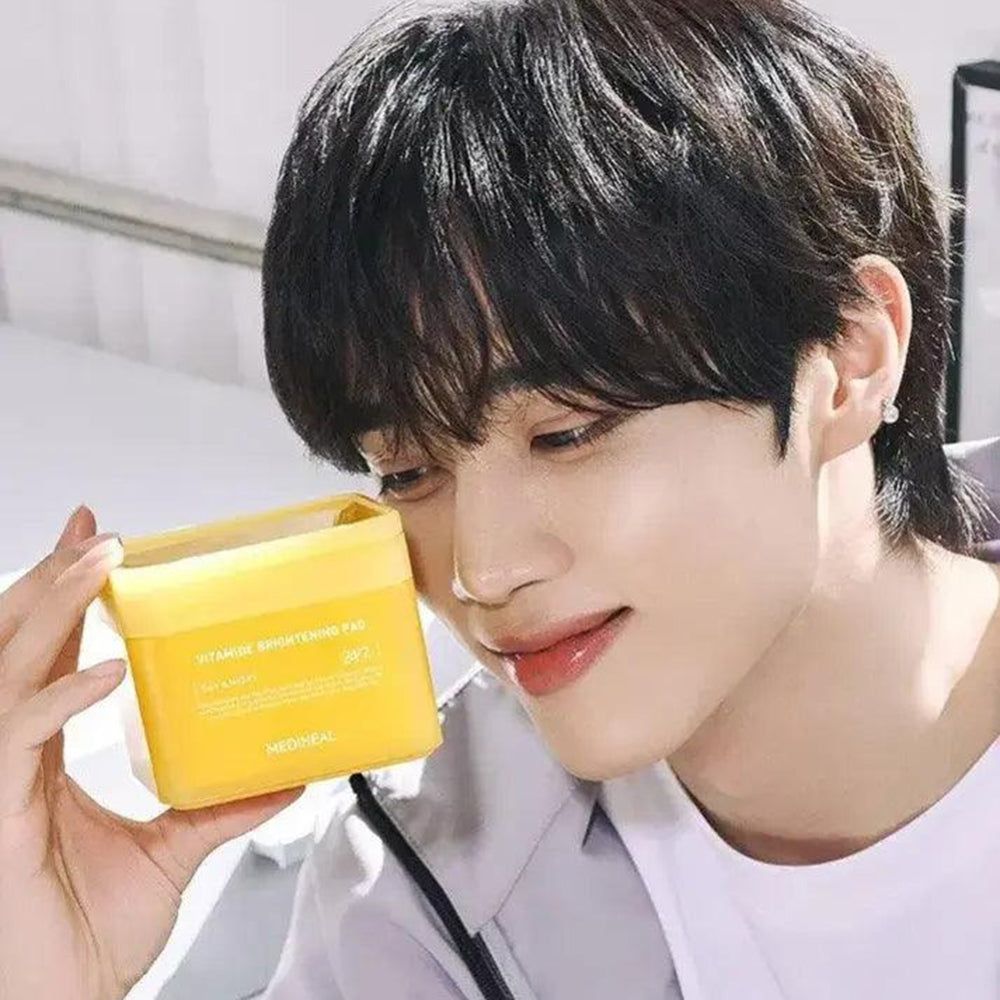 Un uomo tiene in mano una scatola gialla con la scritta Vitamide Brightening Pad. Sorride.