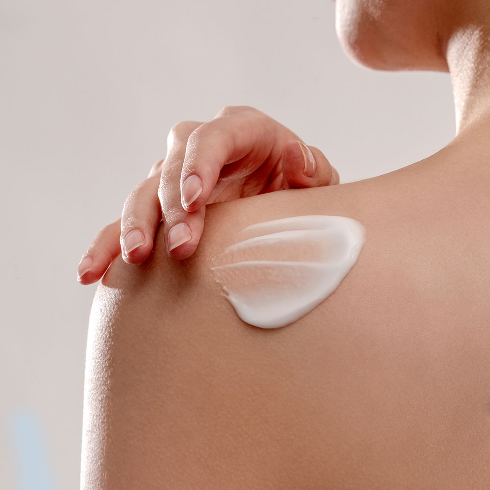 Lozione bianca applicata sulla spalla. Persona con pelle chiara, braccio e spalla visibili.
