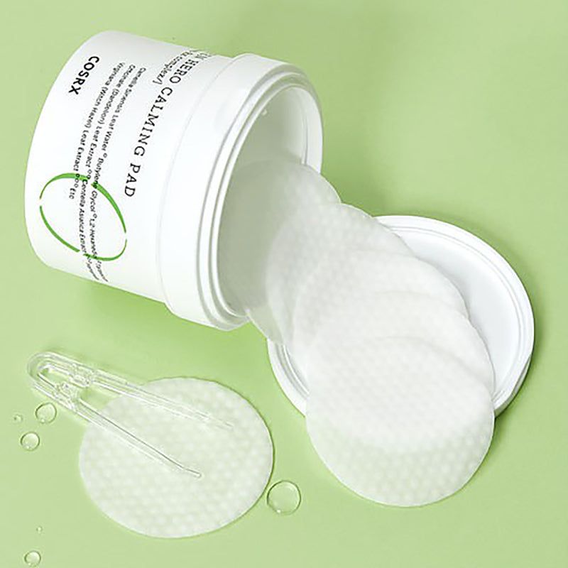 Contenitore bianco aperto con tamponi che cadono. Scritta: Green Hero Calming Pad, COSRX. Sfondo verde.