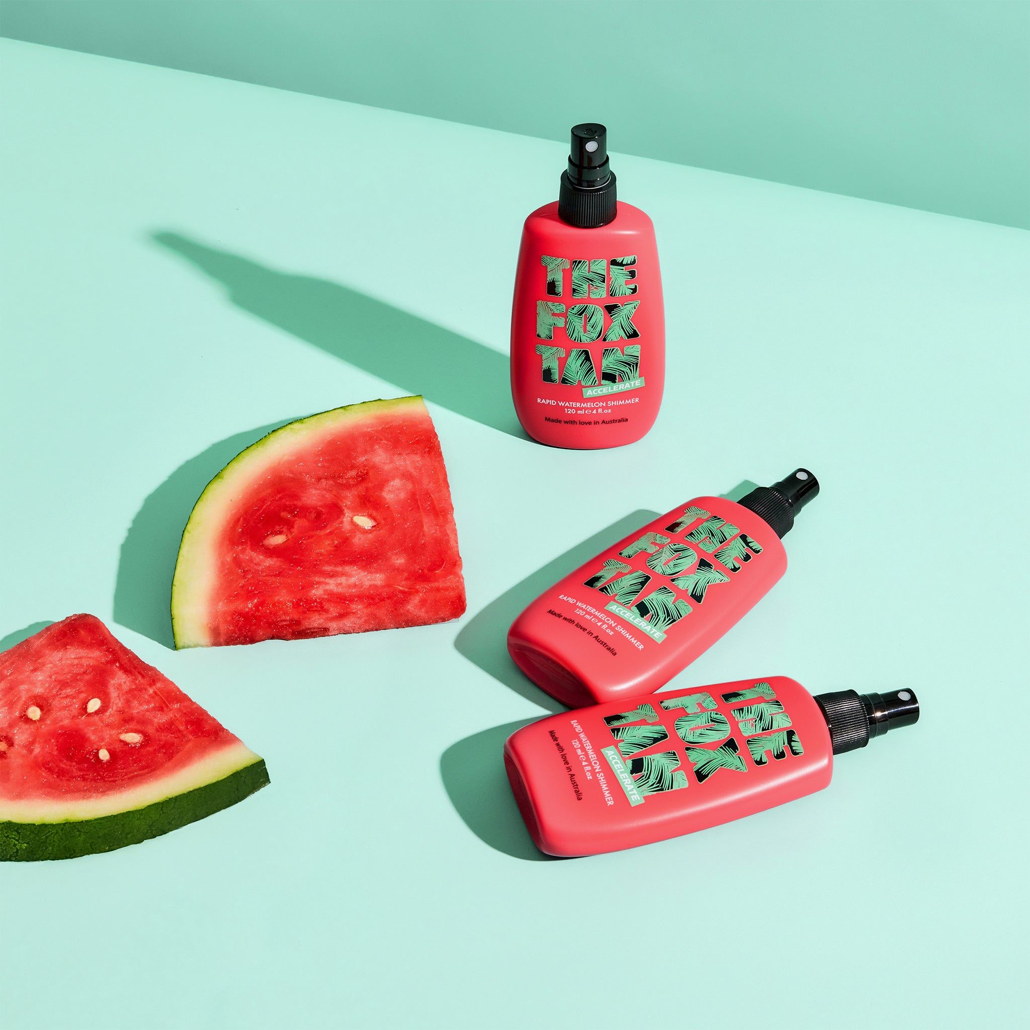 Tre flaconi rosa con vaporizzatore e pezzi di anguria. Scritta: The Fox Tan. Su sfondo blu.