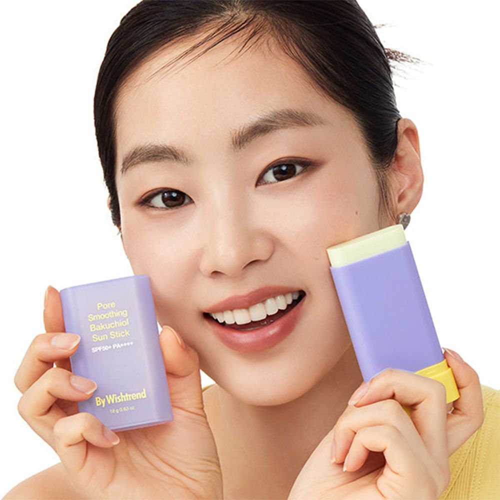 Donna tiene due stick solari viola e gialli. Scritta: Pore Smoothing Bakuchiol Sun Stick SPF50+ PA++++. Marchio: By Wishtrend. Sorride.