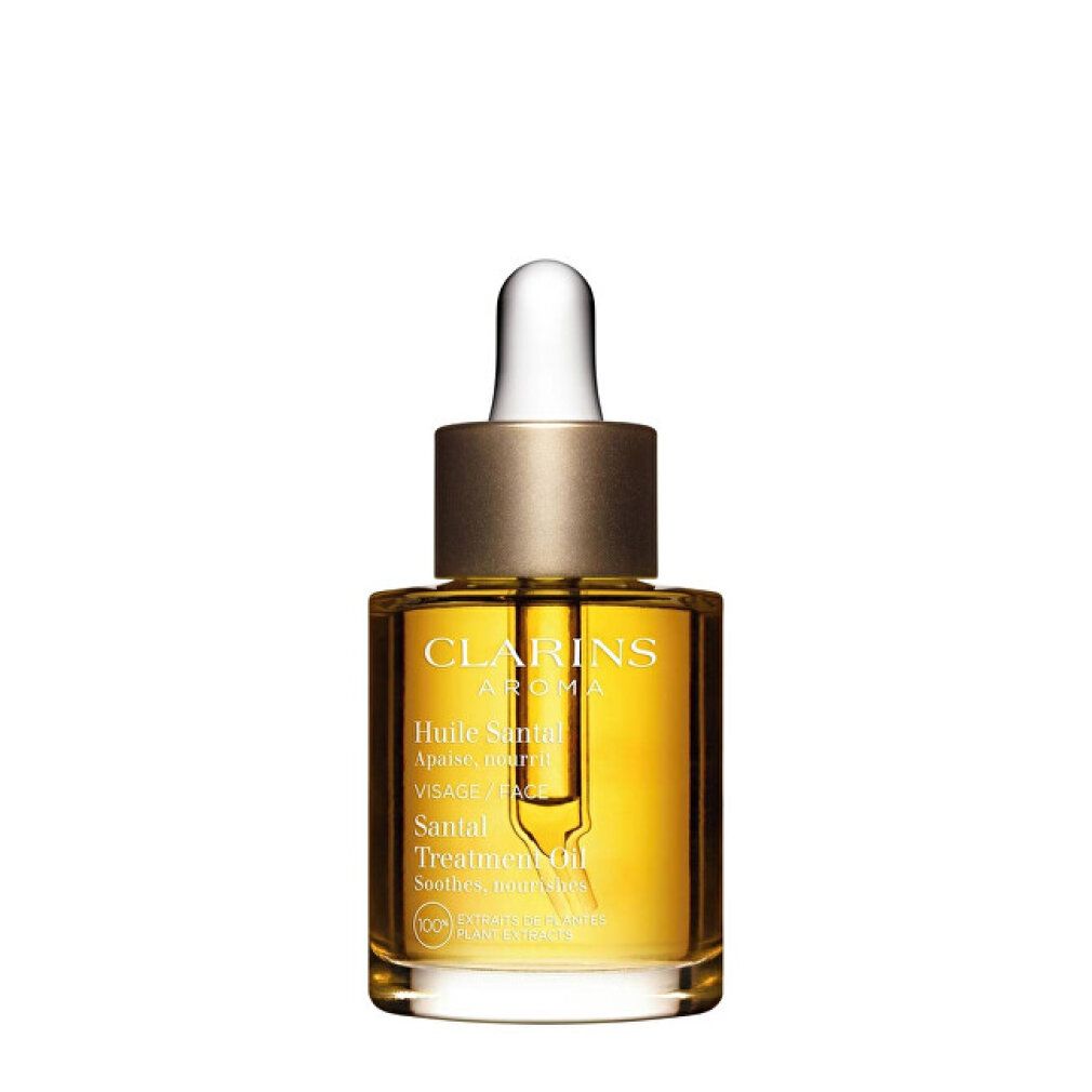 Flacone in vetro con olio dorato e contagocce. Testo: CLARINS Aroma, Huile Santal, Santal Treatment Oil. Tappo dorato.