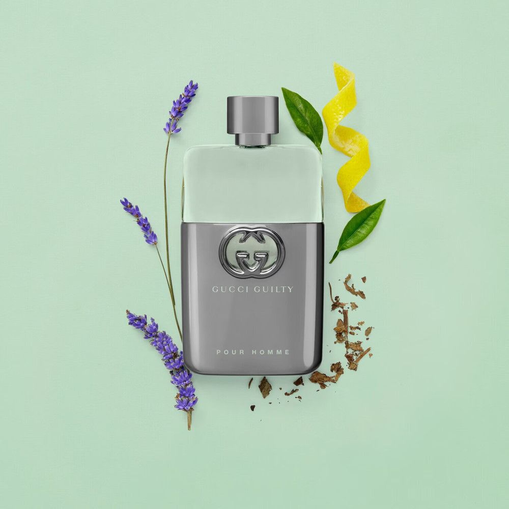 Flacone di Gucci Guilty Pour Homme. Flacone con logo. Circondato da lavanda, foglie e scorze di limone su sfondo verde.