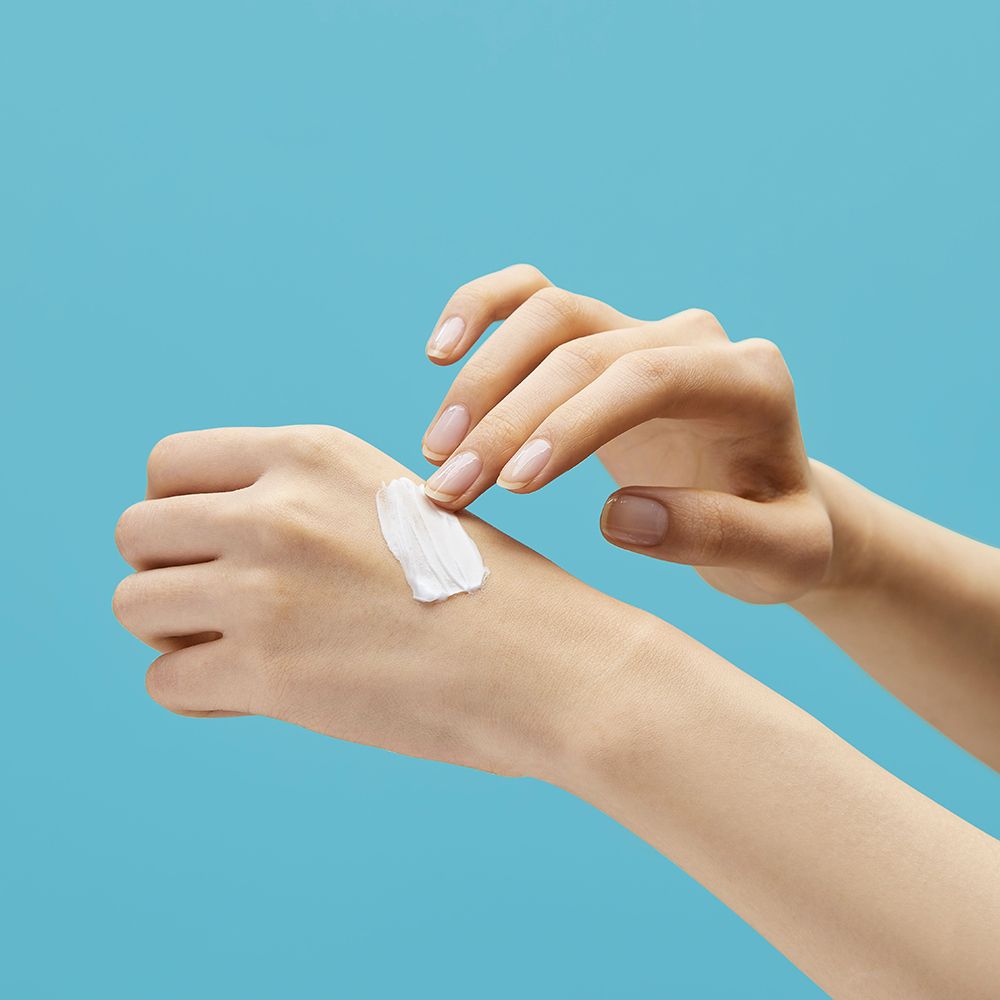 Mani con crema sulla pelle. Macchia di crema sul dorso della mano. Pelle chiara. Sfondo blu.