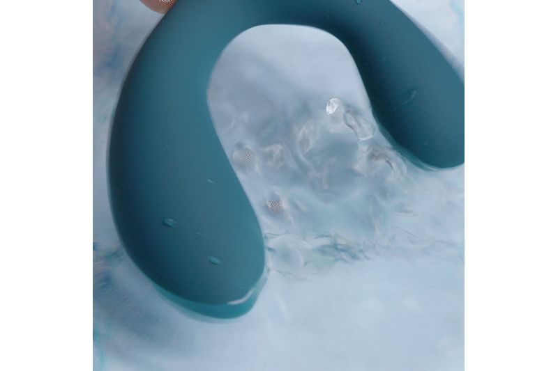Vibratore blu-verde nell'acqua. A forma di U, con estremità arrotondate. L'acqua circonda il prodotto.