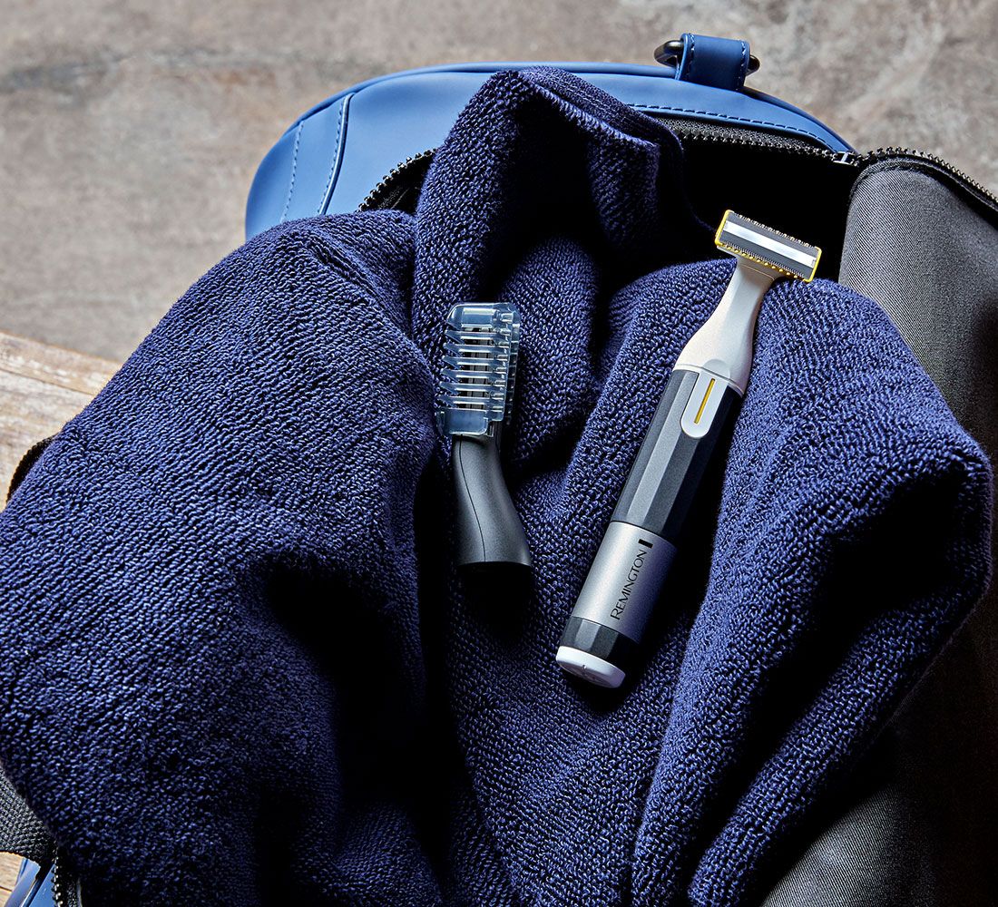 Trimmer e accessorio su un asciugamano blu in una borsa blu. Il trimmer ha una sezione argentata con il marchio Remington.