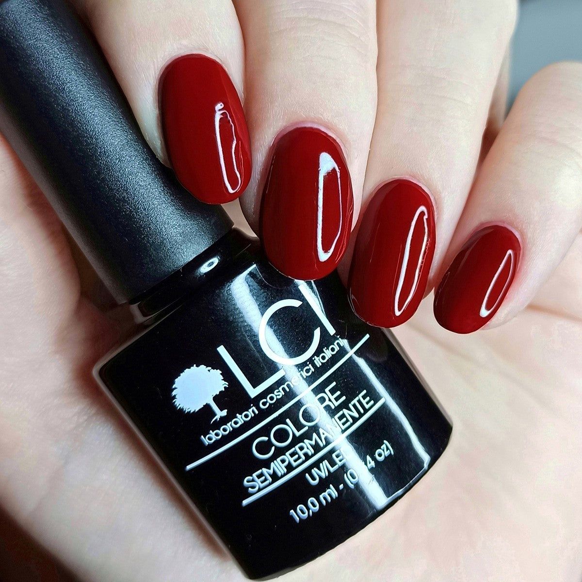 Mano con unghie smaltate e flacone di smalto. Scritta: LCI, Colore Semipermanente, UVLED.