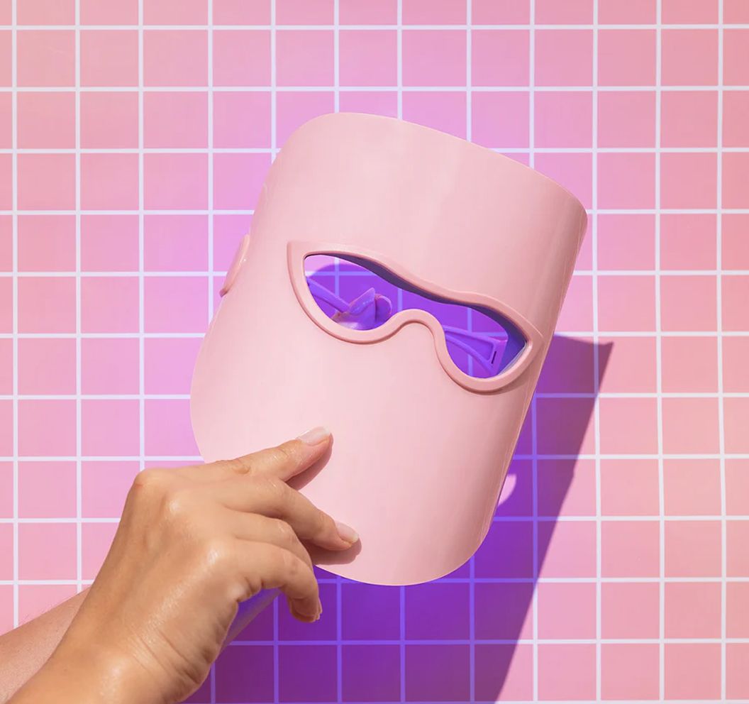 Una maschera LED rosa tenuta in mano davanti a uno sfondo a quadretti.