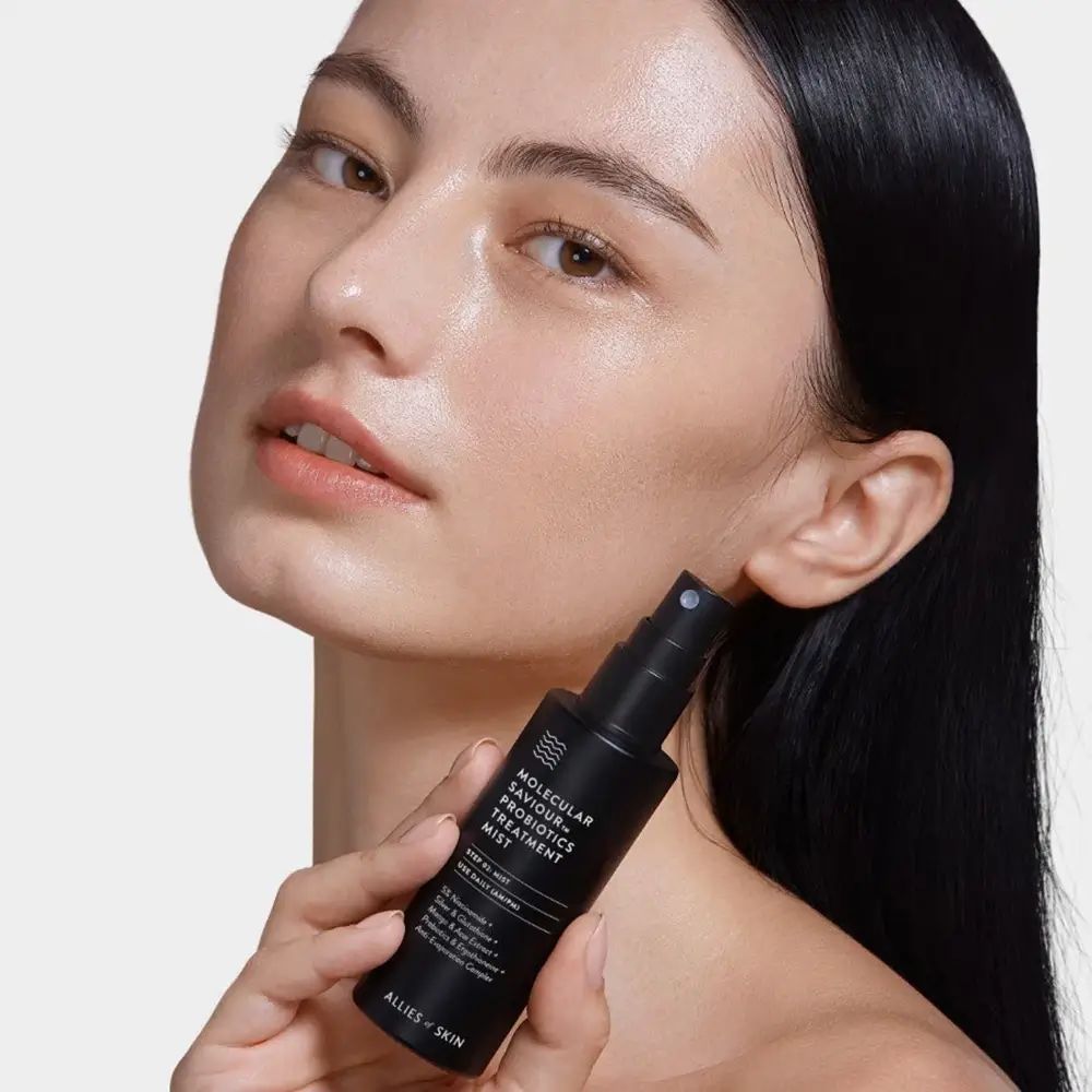 Donna con flacone spray nero. Scritta: Molecular Saviour Probiotics Treatment Mist. Marchio: ALLIES OF SKIN.