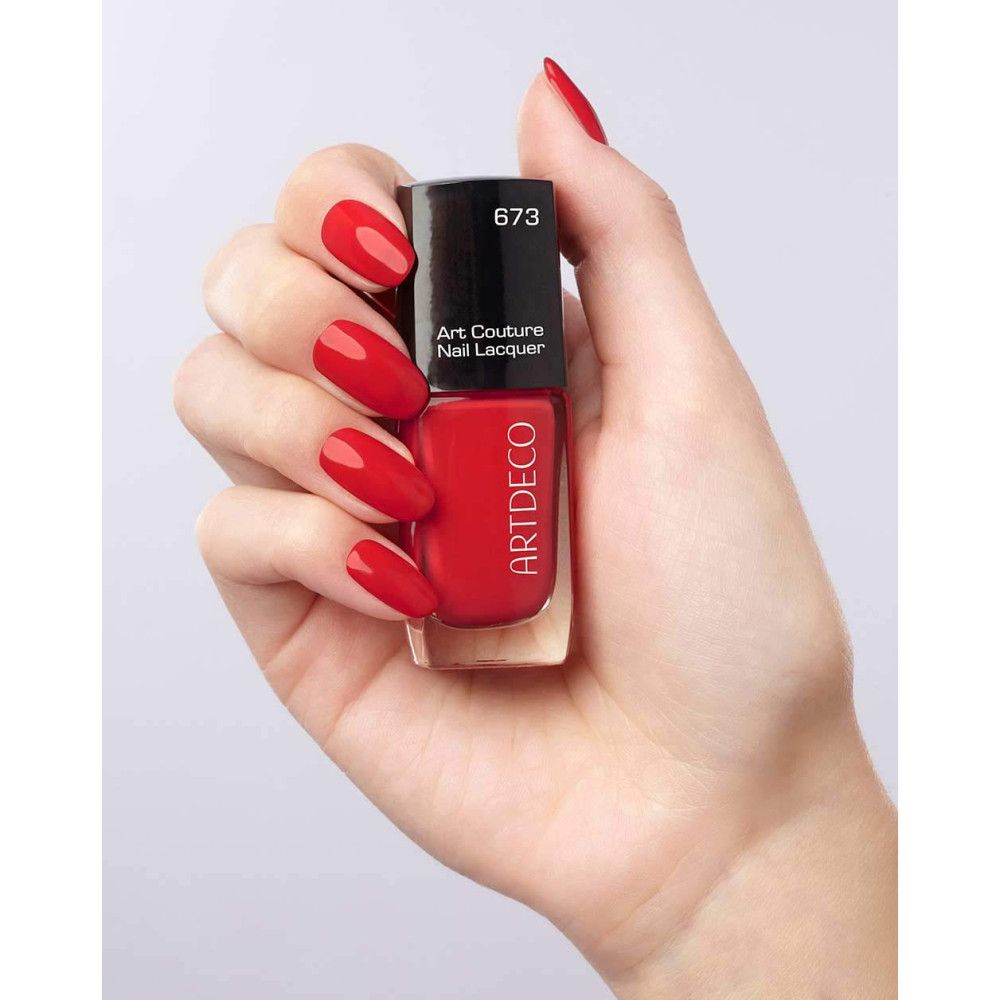 Flacone di smalto rosso Artdeco in mano. Scritta: Art Couture Nail Lacquer, 673. Unghie smaltate abbinate.