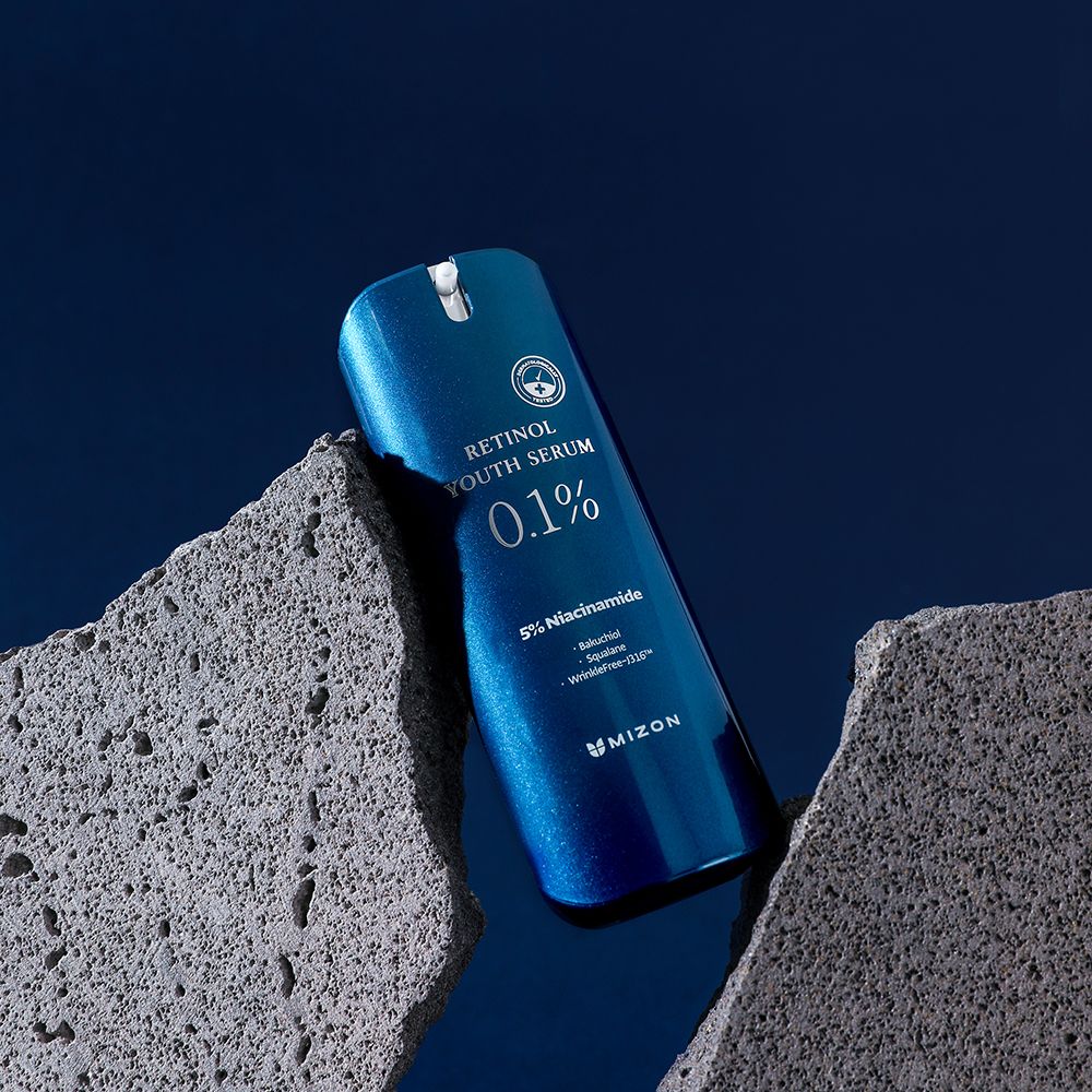 Flacone di siero blu, parzialmente nascosto da pietre. Scritta: Retinol Youth Serum 0.1%, 5% Niacinamide, MIZON.