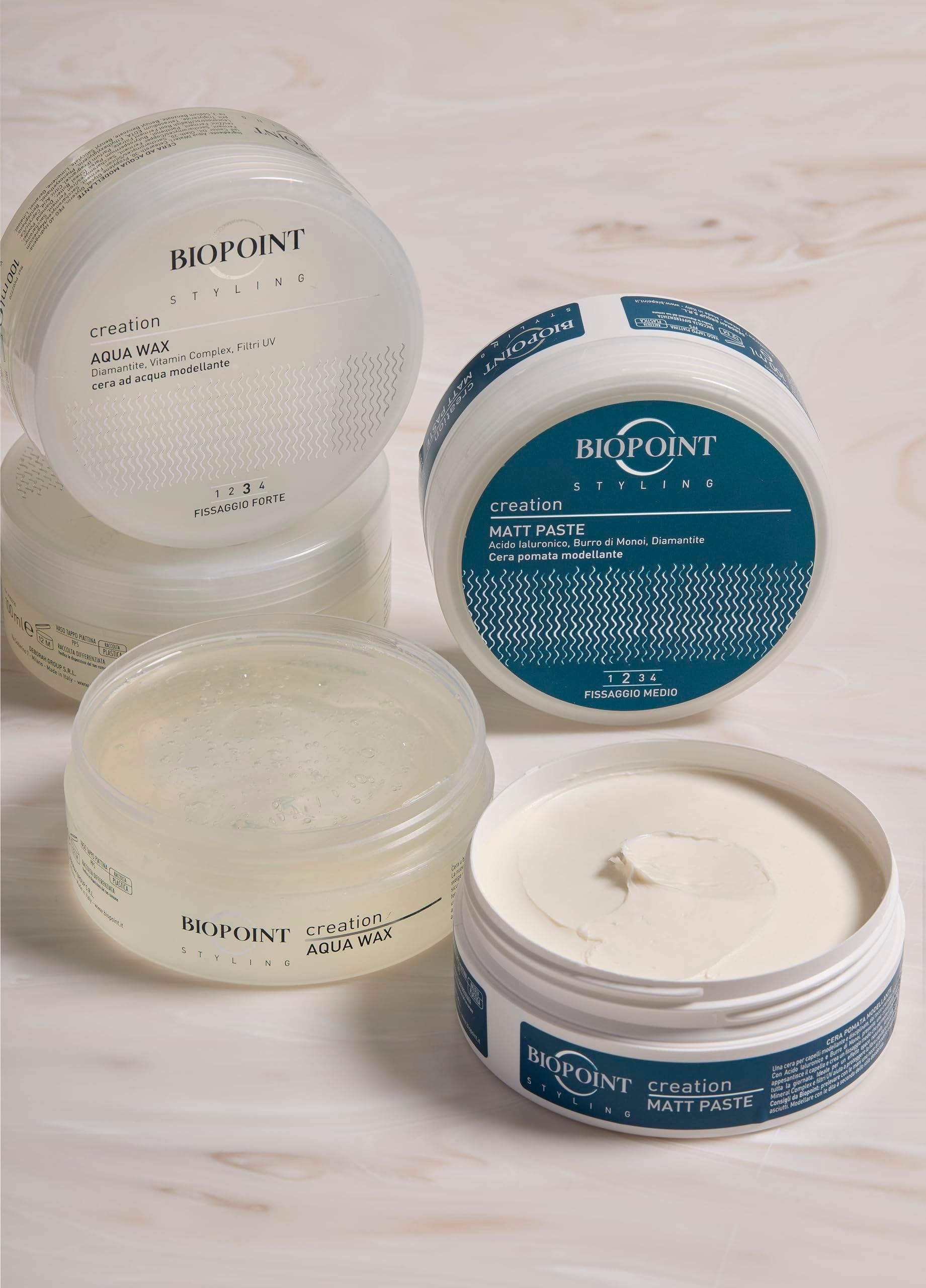 Diversi barattoli trasparenti con coperchi. Scritta "BIOPOINT creation AQUA WAX" e "MATT PASTE". Barattolo aperto con contenuto bianco.