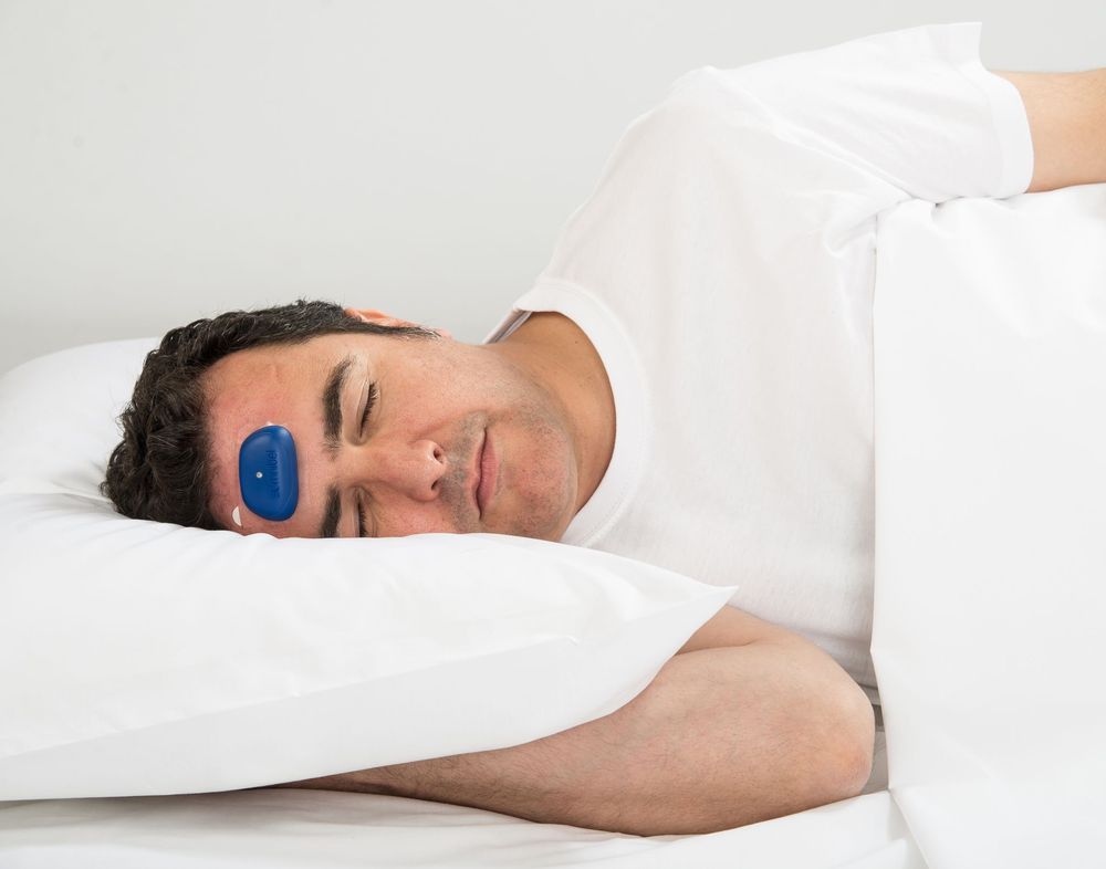 Uomo a letto con dispositivo blu sulla fronte. Sdraiato su un cuscino.