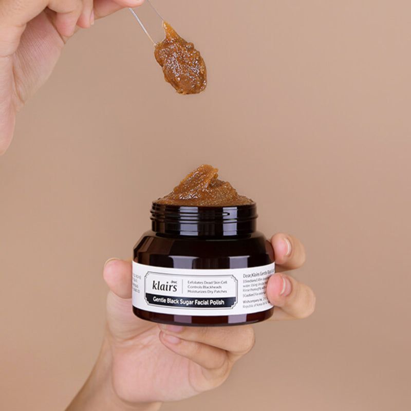 Pasta esfoliante allo zucchero marrone in un barattolo. Un cucchiaio ne contiene una porzione. Scritta: Dear Klairs Gentle Black Sugar Facial Polish.