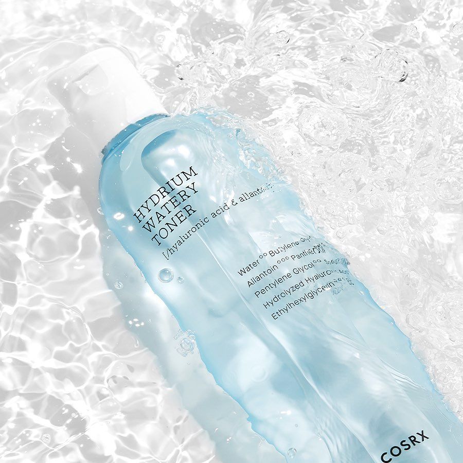 Flacone di toner per la pelle, liquido blu, tappo bianco. L'acqua circonda il flacone. Scritte: HYDRIUM WATERY TONER, ingredienti. Marchio COSRX.