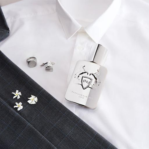 Flacone argentato su camicia bianca. Gemelli e accessori. Flacone con logo e scritta 'Parfums de Marly'.