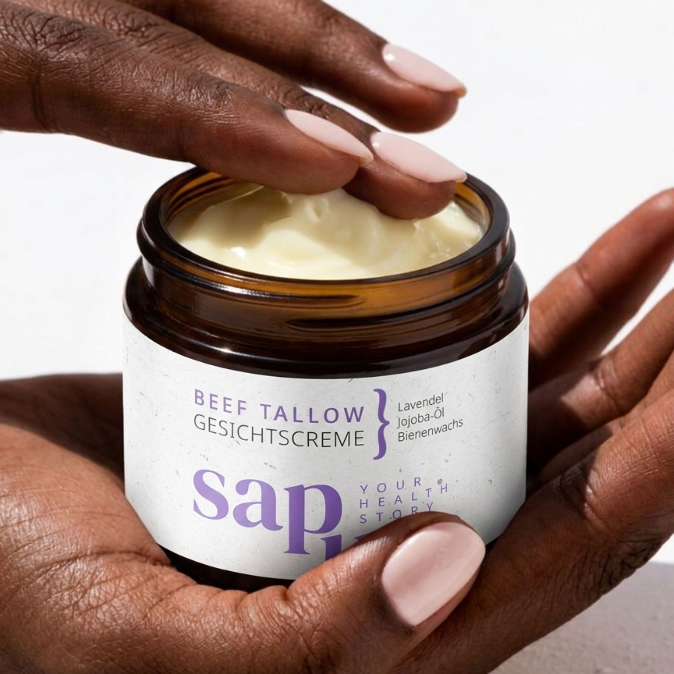 Mani che tengono un vasetto di crema. Scritta: BEEF TALLOW GESICHTSCREME, Lavanda, Olio di jojoba, Cera d'api. Marchio: sapura.