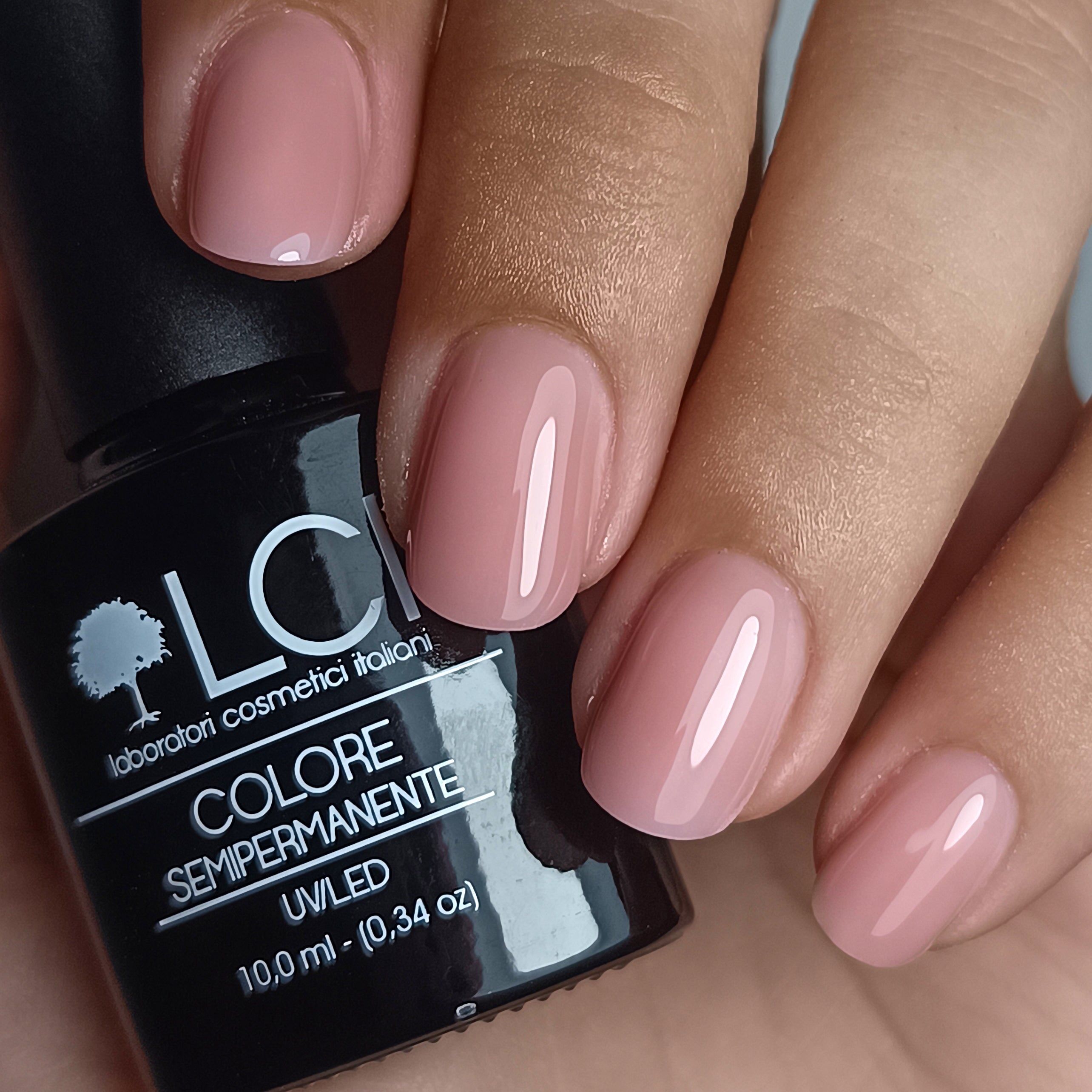 Flacone di smalto accanto a unghie smaltate. Flacone con logo e nome prodotto. Unghie ovali, smalto rosa.