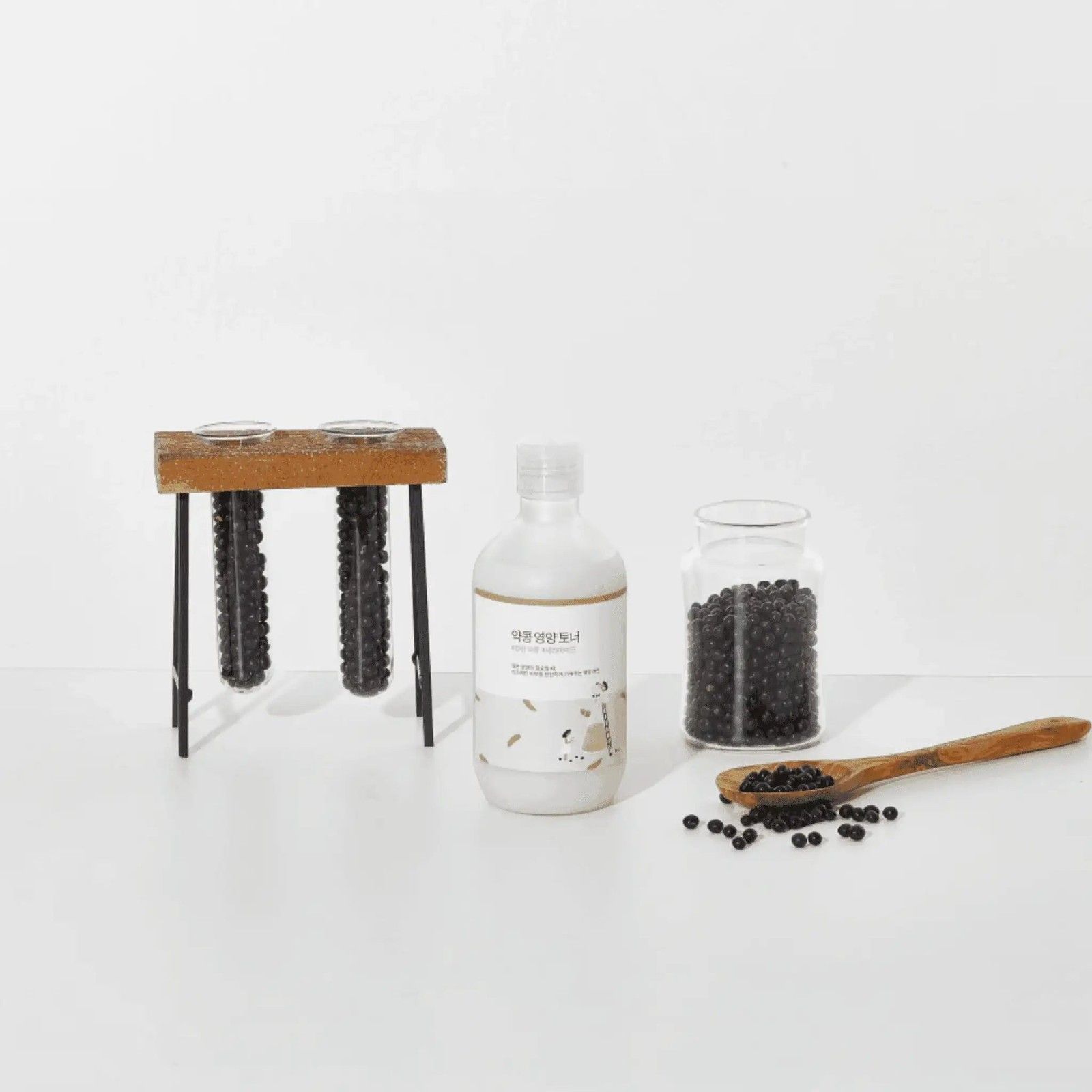 Flacone di ROUND LAB Soy Bean Nourishing Toner accanto a un barattolo di soia e un cucchiaio di legno.