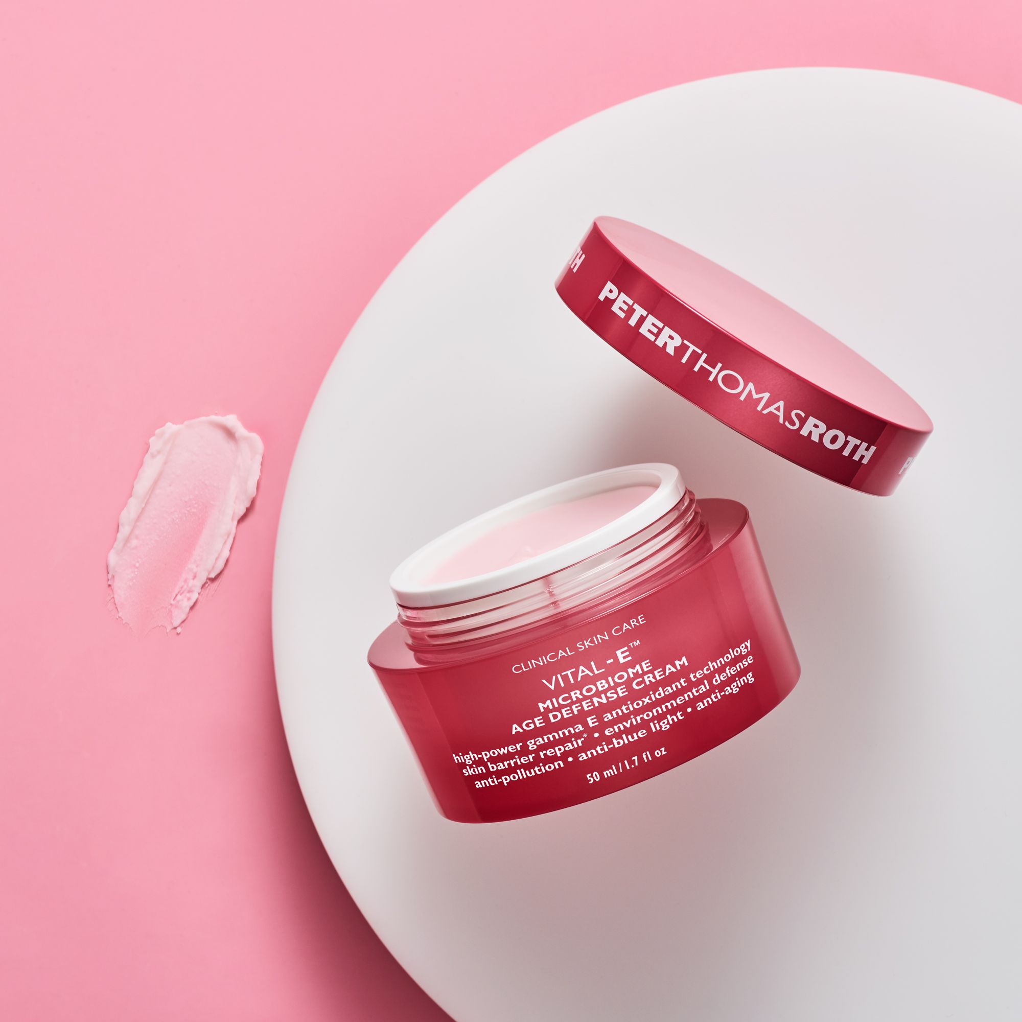 Vaso di crema rosa aperto con coperchio accanto. Scritta: Peter Thomas Roth, Vital-E Microbiome Age Defense Cream.