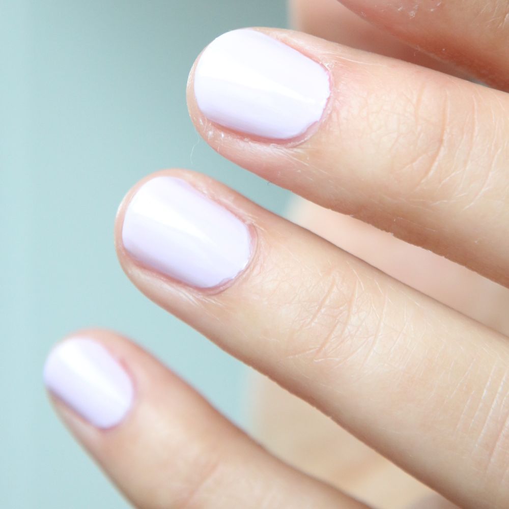 Primo piano di dita con smalto lilla chiaro. Le unghie sono corte e smaltate.