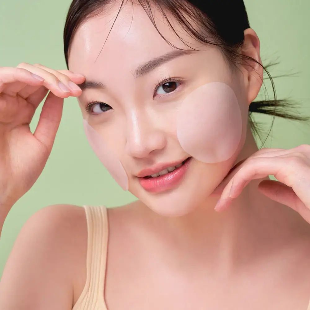 Donna con cuscinetti sulle guance. I cuscinetti sono rotondi e trasparenti. Sfondo verde.